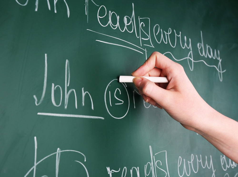 teacher highlighting parts of a sentence on a chalkboard to show how to teach grammar to children